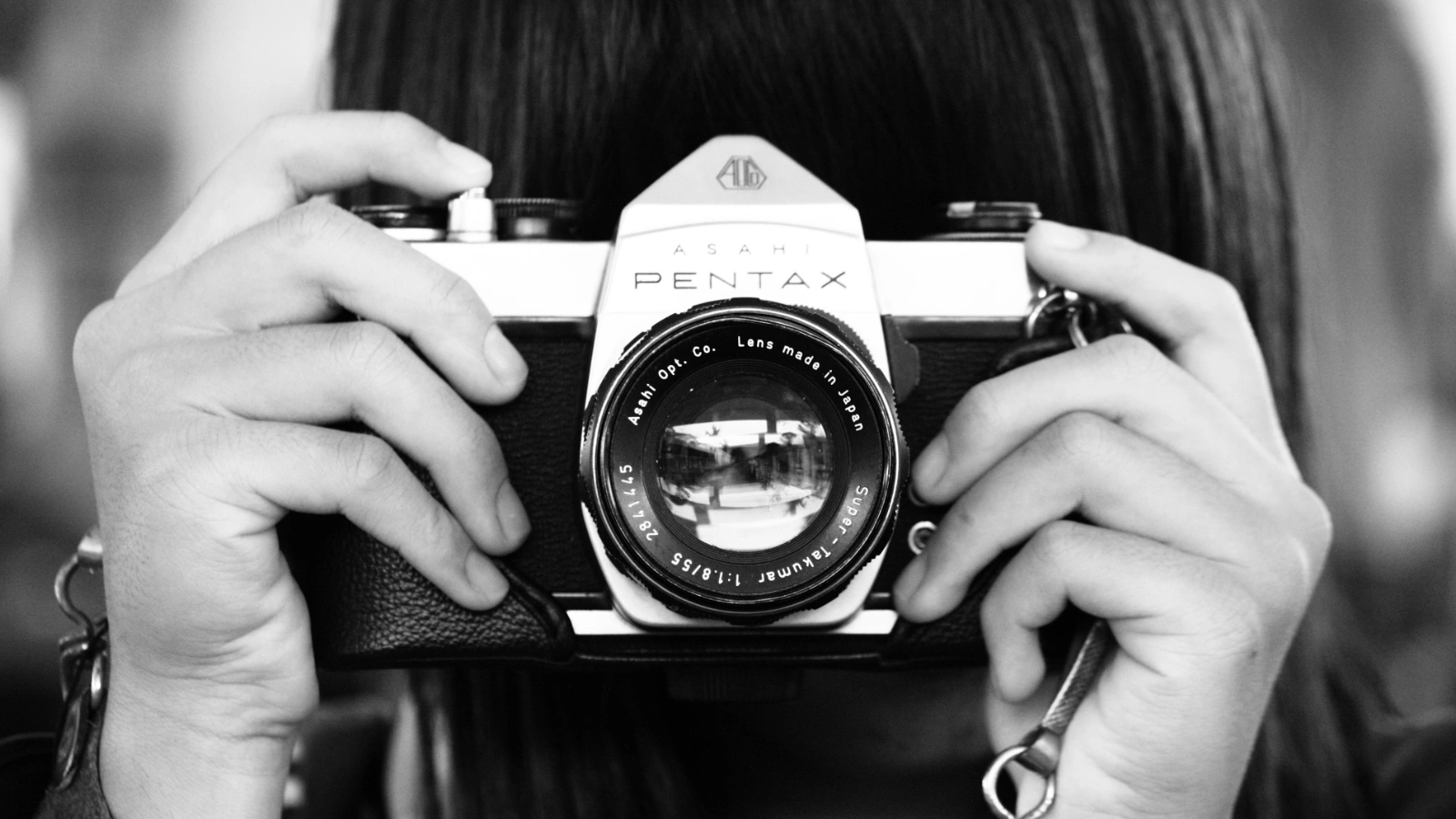 Black and white photo of hands holding a vintage Pentax camera, symbolizing the art of commercial photography tailored to a client's vision.